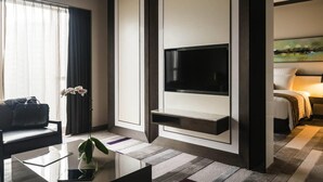 Ein modernes Hotelzimmer mit flachbildfernseher an der Wand, einer Couch, einem Couchtisch und einem Gemälde.