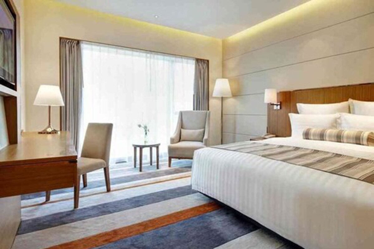 A hotel room with a large bed, two chairs, a desk, and a small table.