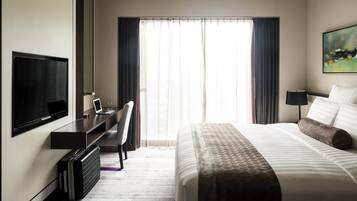 A hotel room with a bed, a desk with a laptop, a TV, and a large window with curtains.