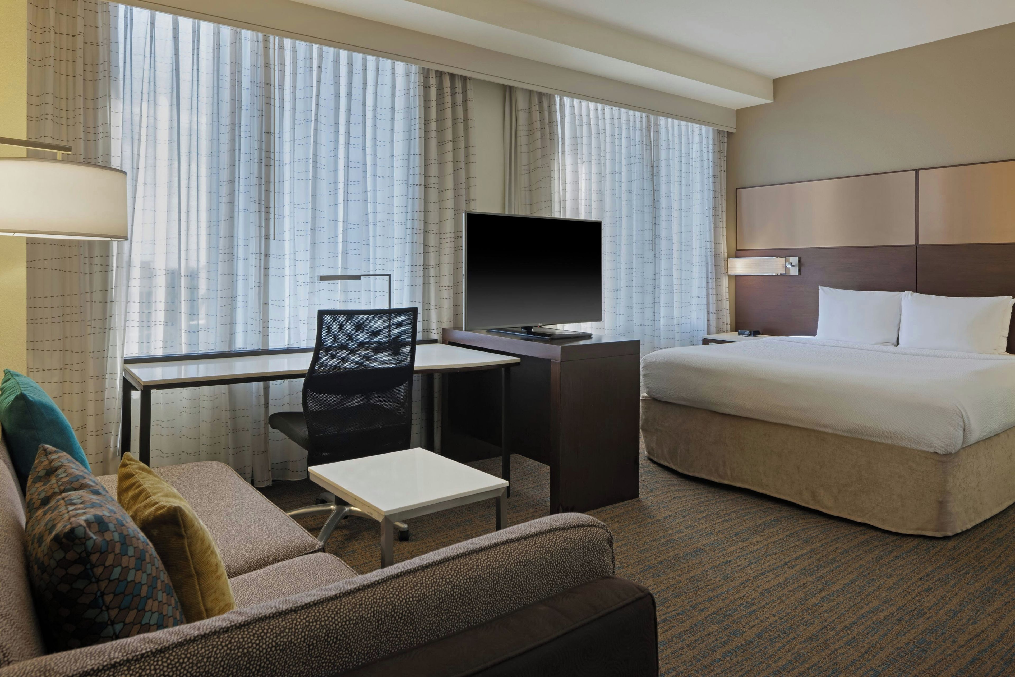 Ein Hotelzimmer mit einem Bett, einem Schreibtisch mit Stuhl, einem Fernseher und einem Sofa.