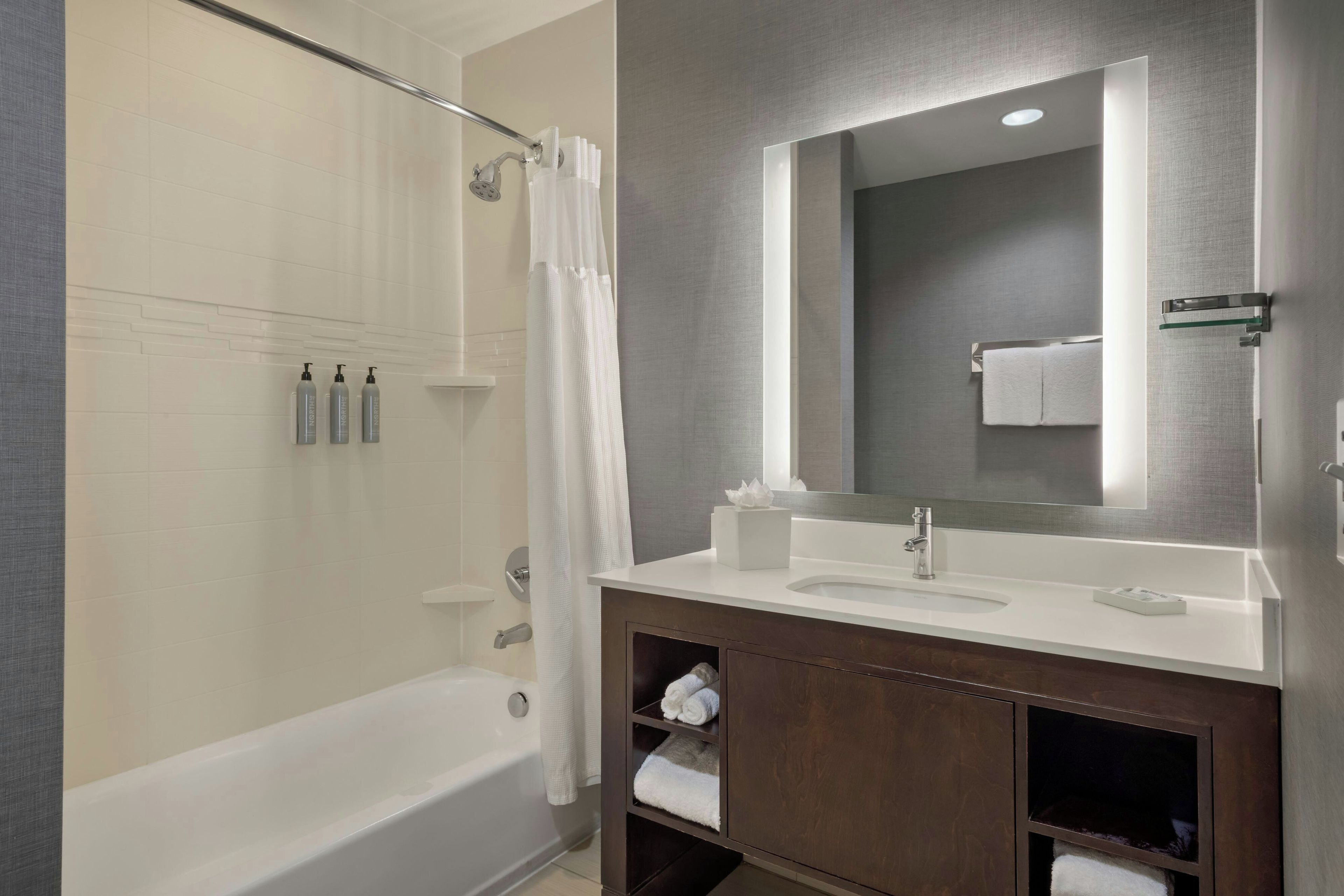 A modern bathroom with a bathtub, a shower, a vanity with a mirror, and toiletries.