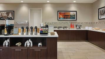 A modern hotel breakfast area with a coffee station, a variety of food options, and artwork on the walls.