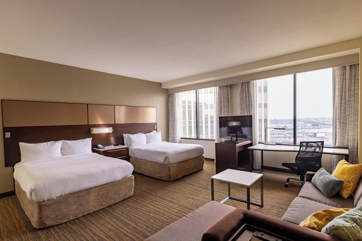 A hotel room with two beds, a desk, a chair, a sofa, and a TV.