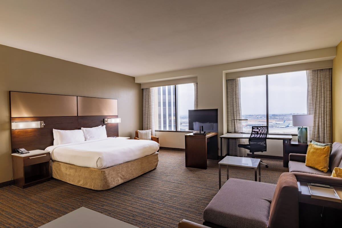 A hotel room with a large bed, a desk, a chair, a sofa, and a TV.