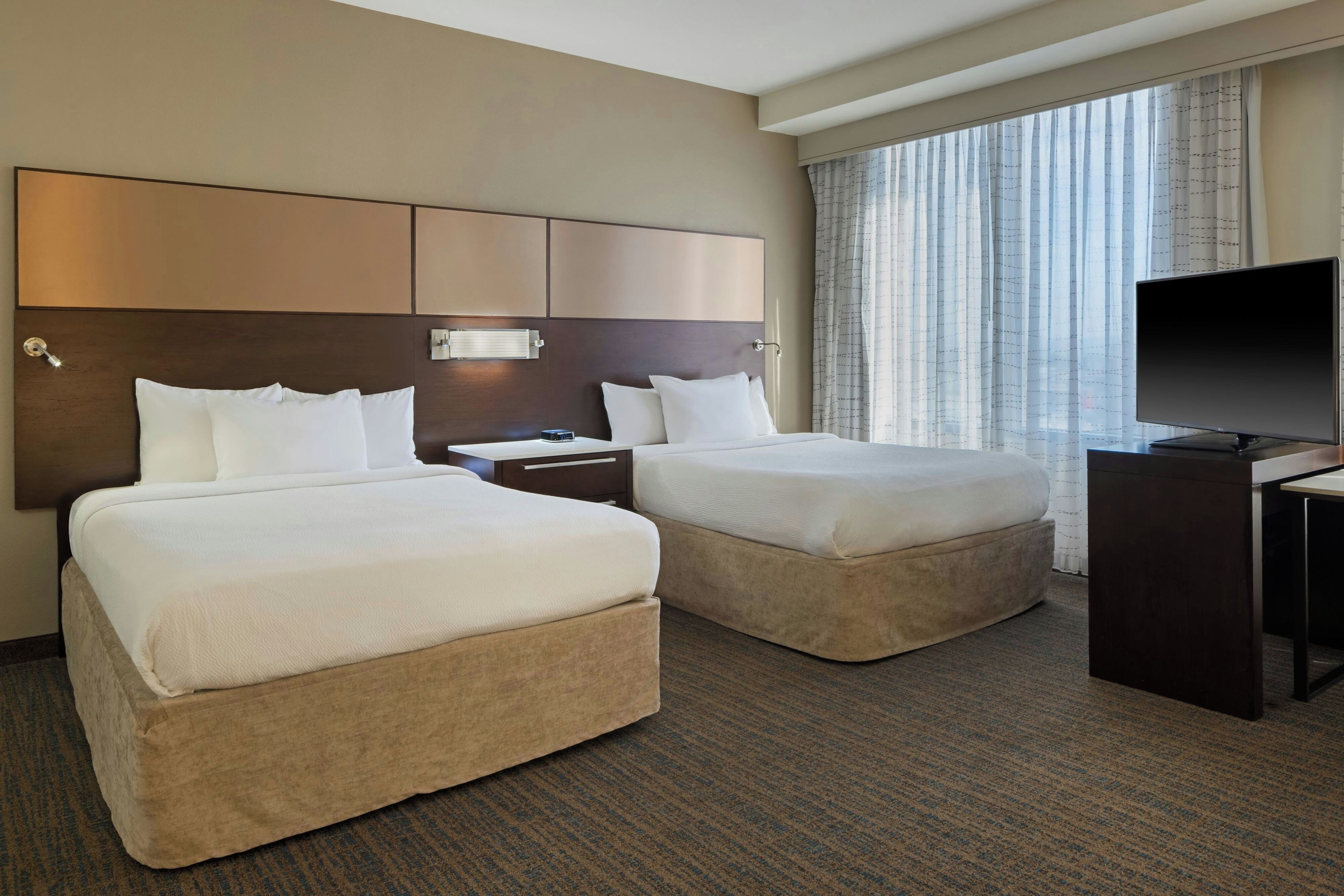 A hotel room with two beds, a television, and a window with curtains.