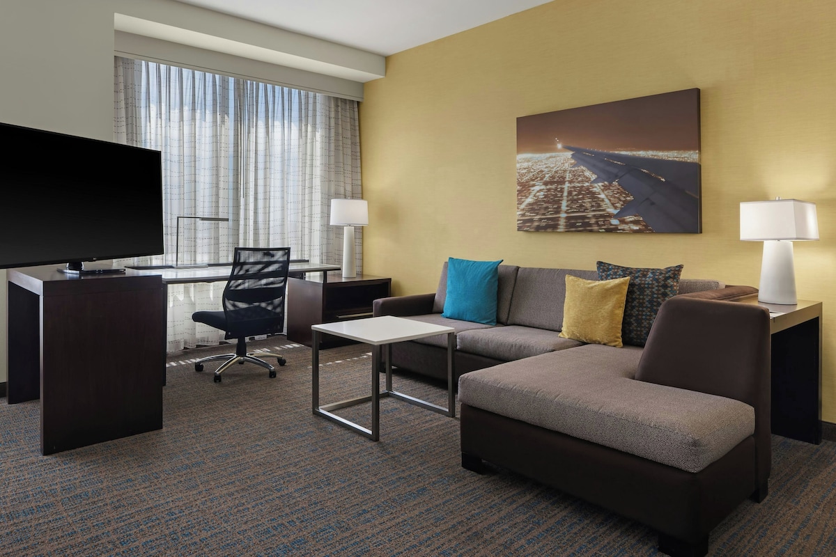 Habitación de hotel con escritorio, silla, sofá y televisor.