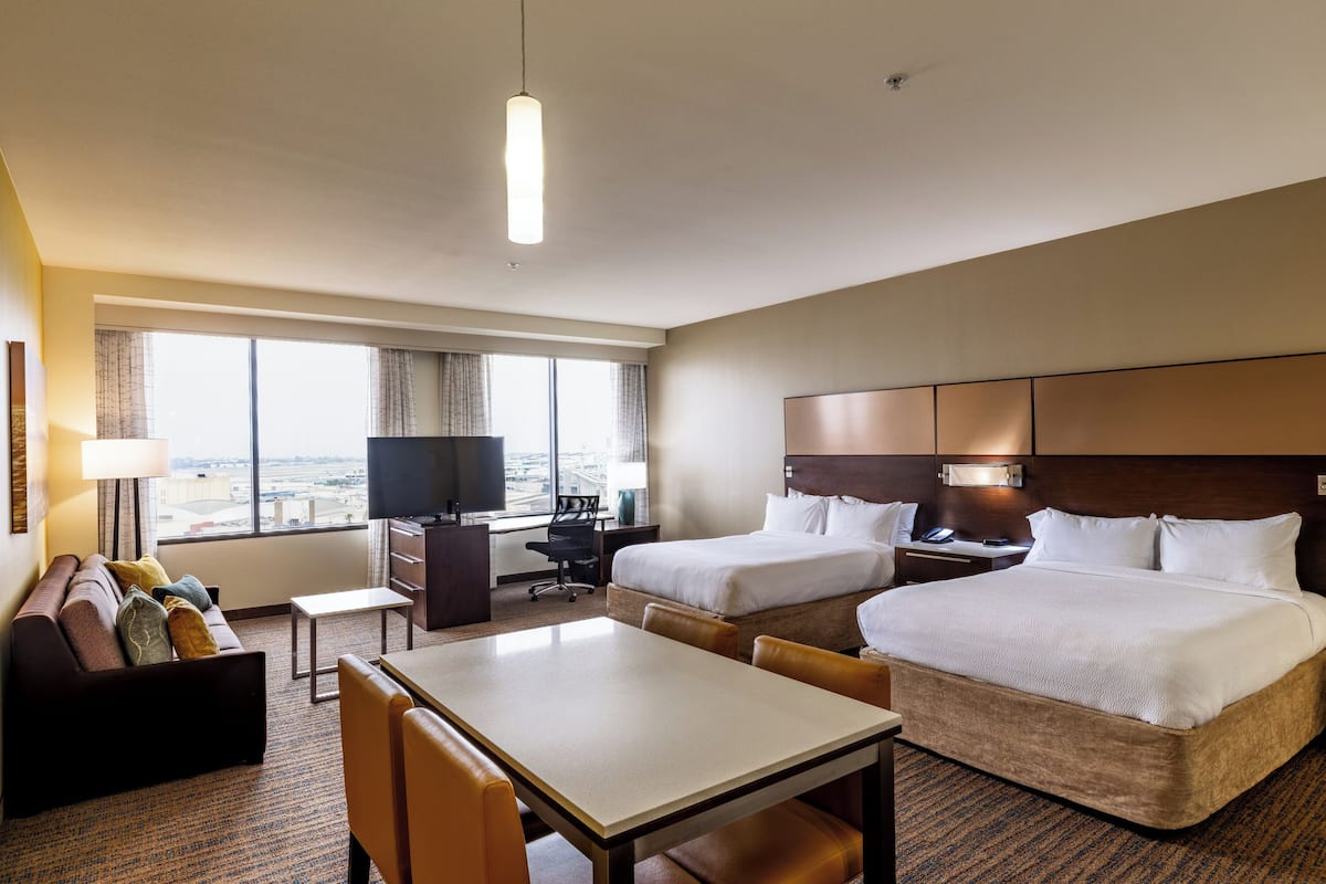 A hotel room with two beds, a desk, a TV, and a view of the city.