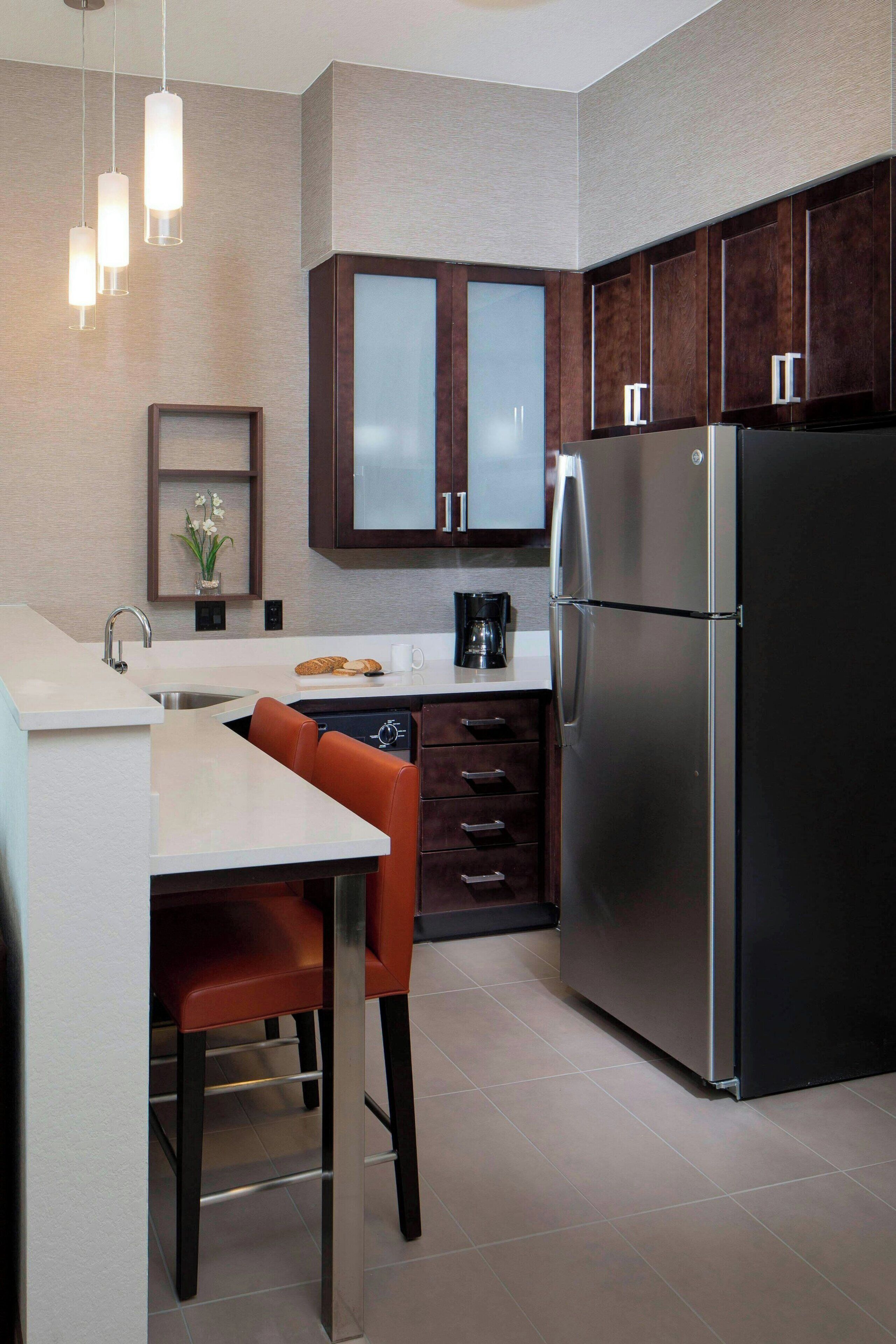 A modern kitchen with a stainless steel refrigerator, dark wooden cabinets, and a white countertop.
