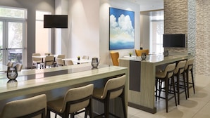 A modern kitchen with a long island, bar stools, and a large painting of clouds. - Residence Inn by Marriott West Palm Beach Downtown (West Palm Beach)