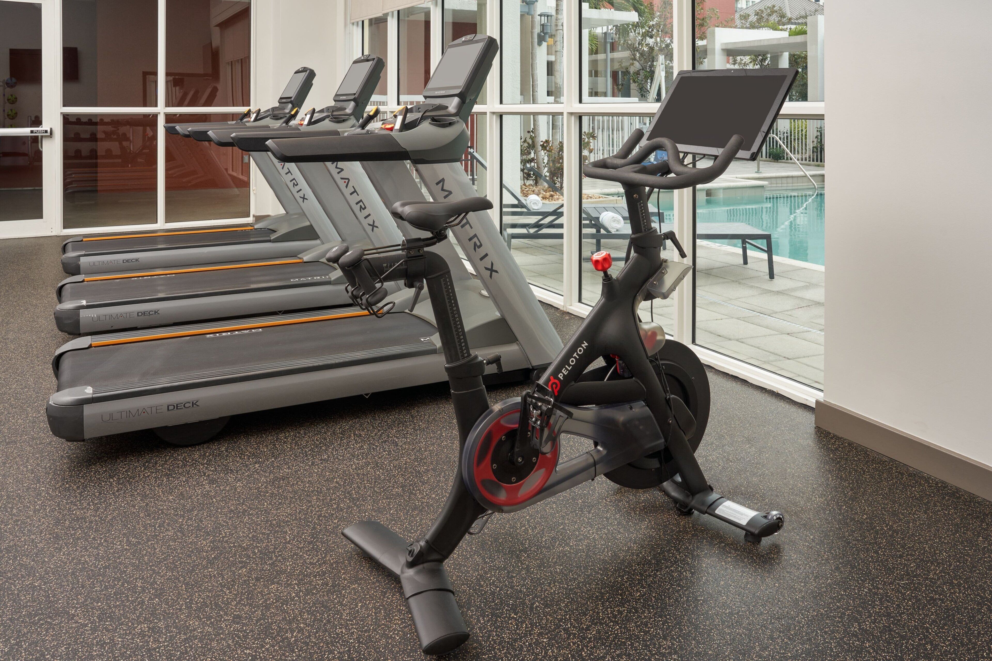 Une salle de sport équipée de vélos d’exercice, de tapis de course et offrant une vue sur une piscine.