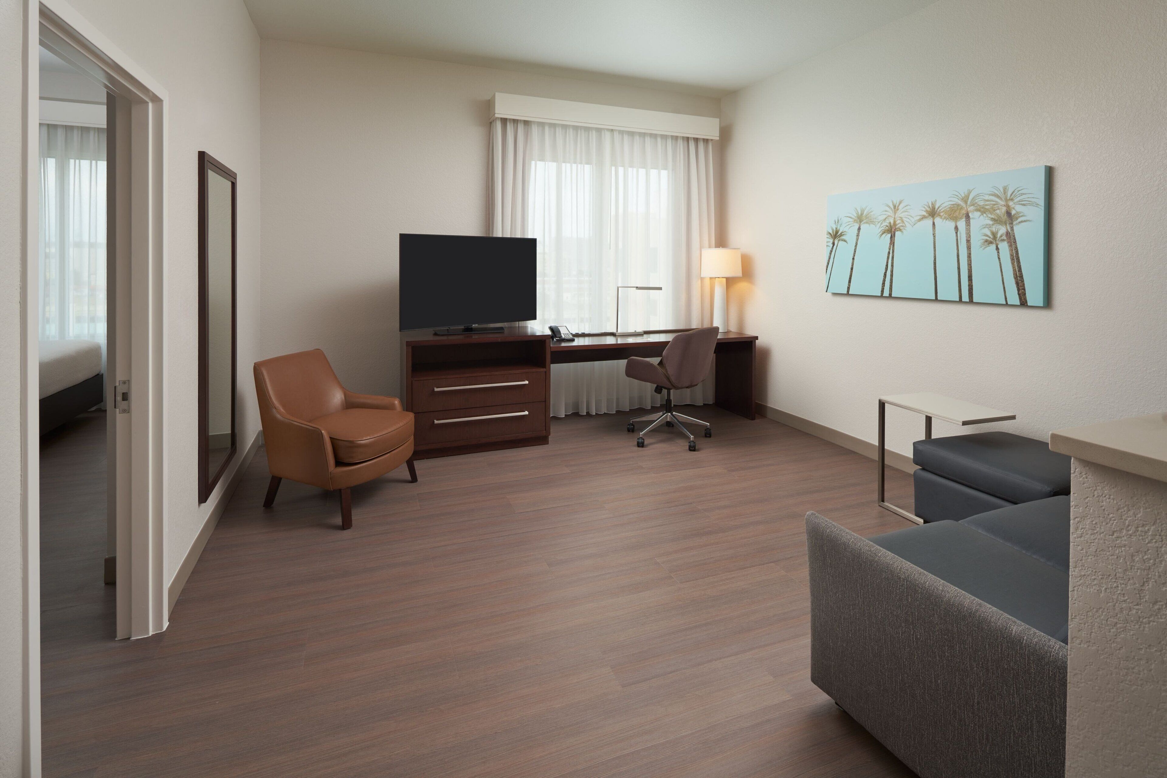 A hotel room with a bed, a desk with a computer, a TV, a chair, a sofa, and a painting on the wall.