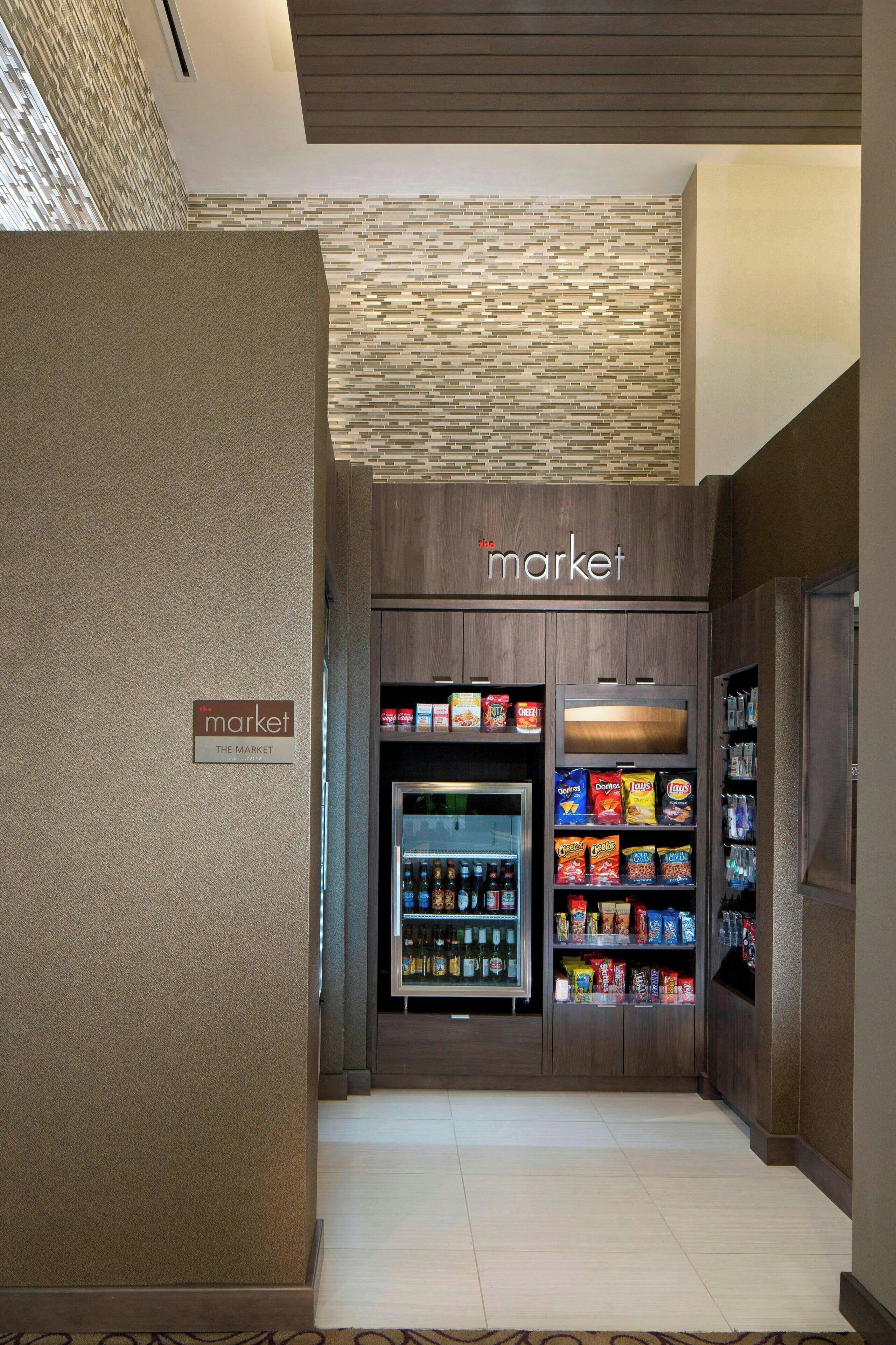A hotel market area with a refrigerated section and shelves stocked with snacks.