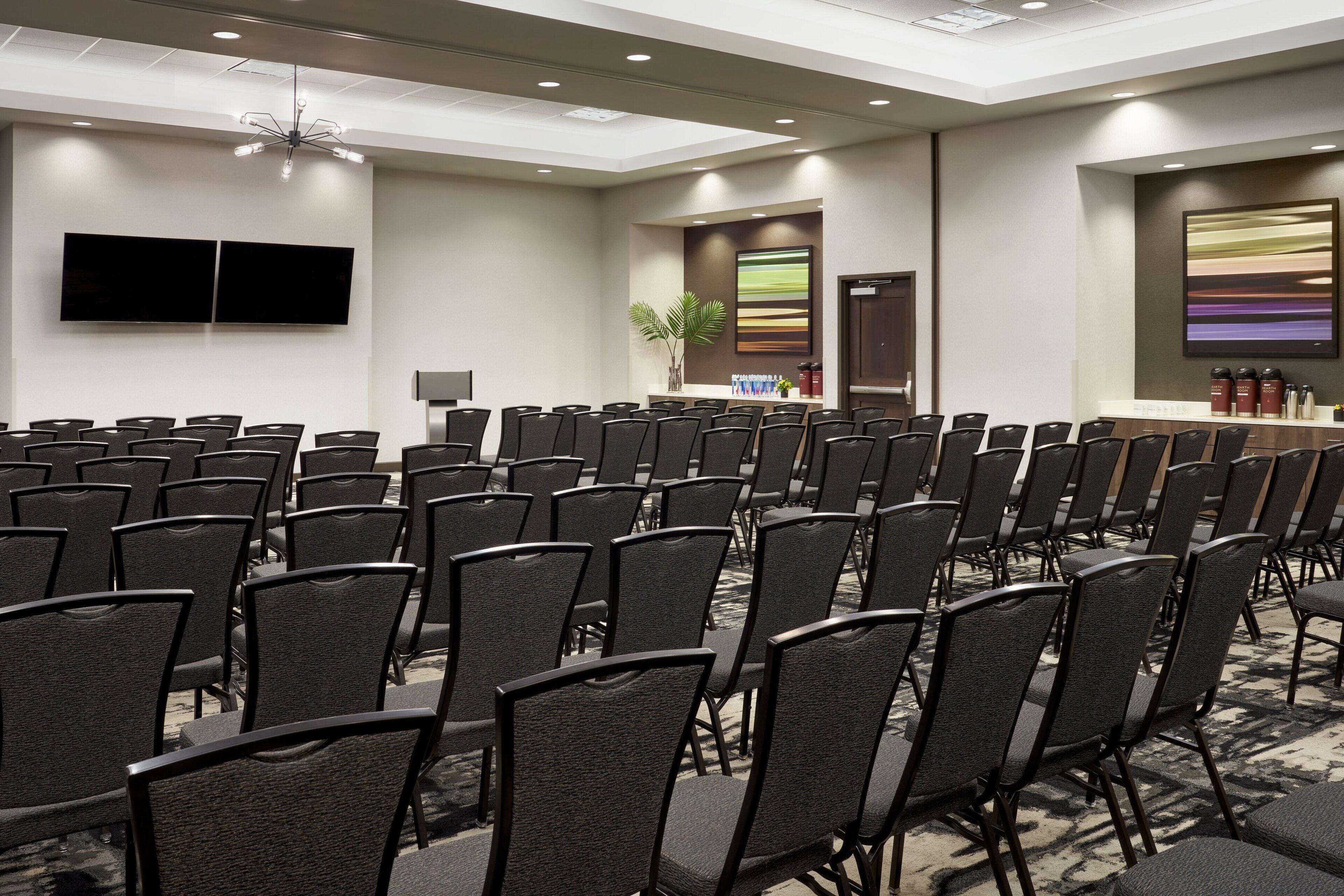 A conference room with rows of chairs, a large screen, and a reception desk.