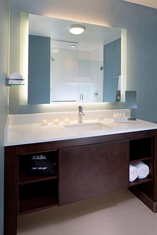 A modern bathroom with a large mirror, white sink, and dark wood vanity.