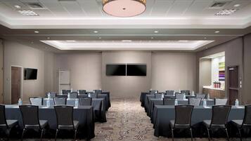 A conference room with tables and chairs, a flat-screen TV, and a carpeted floor.