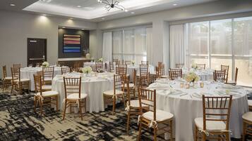 A conference room with round tables, white tablecloths, and wooden chairs.