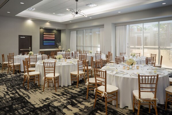 A conference room with round tables, white tablecloths, and wooden chairs.