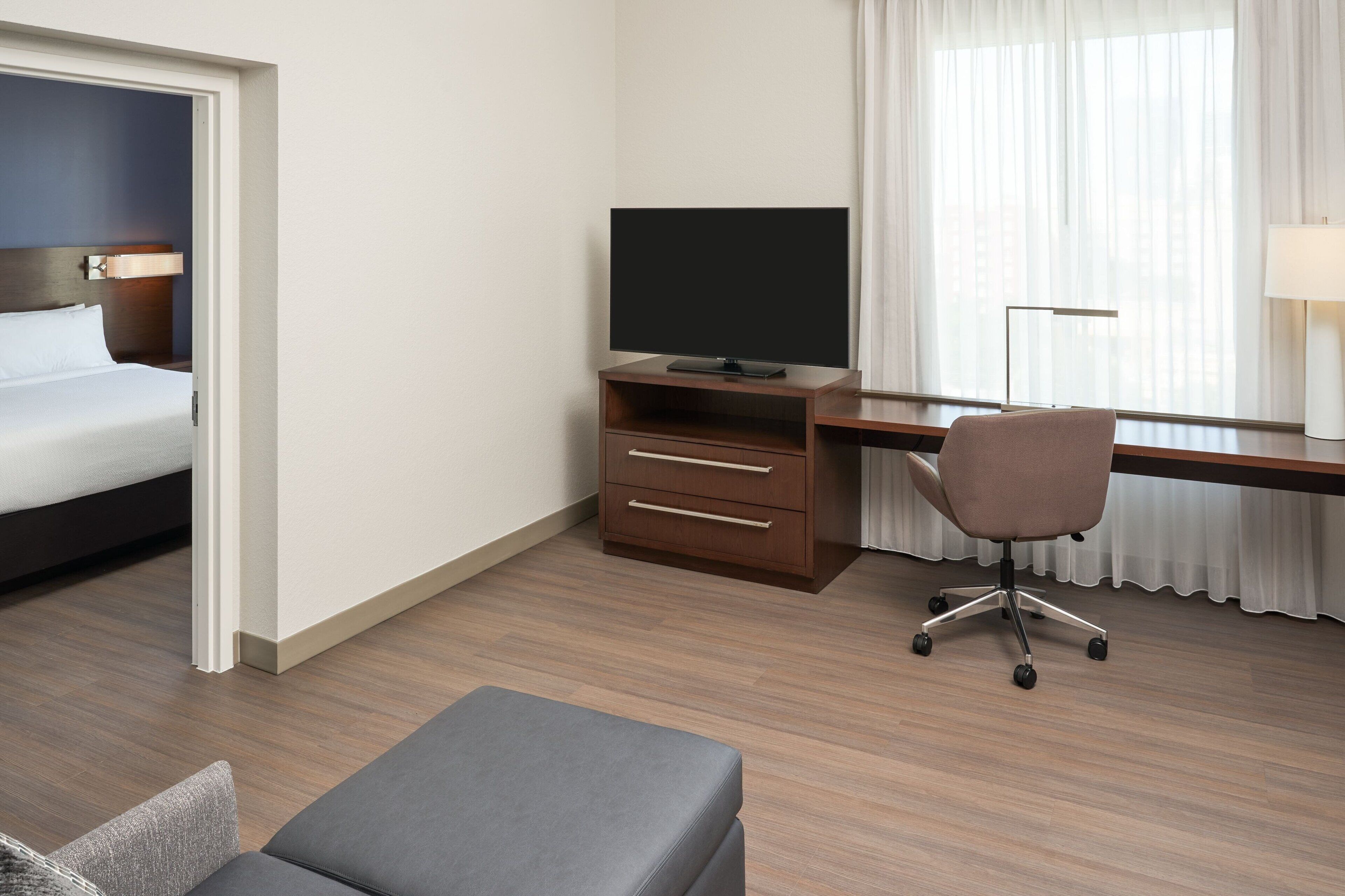 A hotel room with a bed, a desk with a TV, a chair, and a lamp.