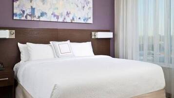 A hotel room with a large bed, a headboard with a light fixture, a nightstand, and a window with sheer curtains.