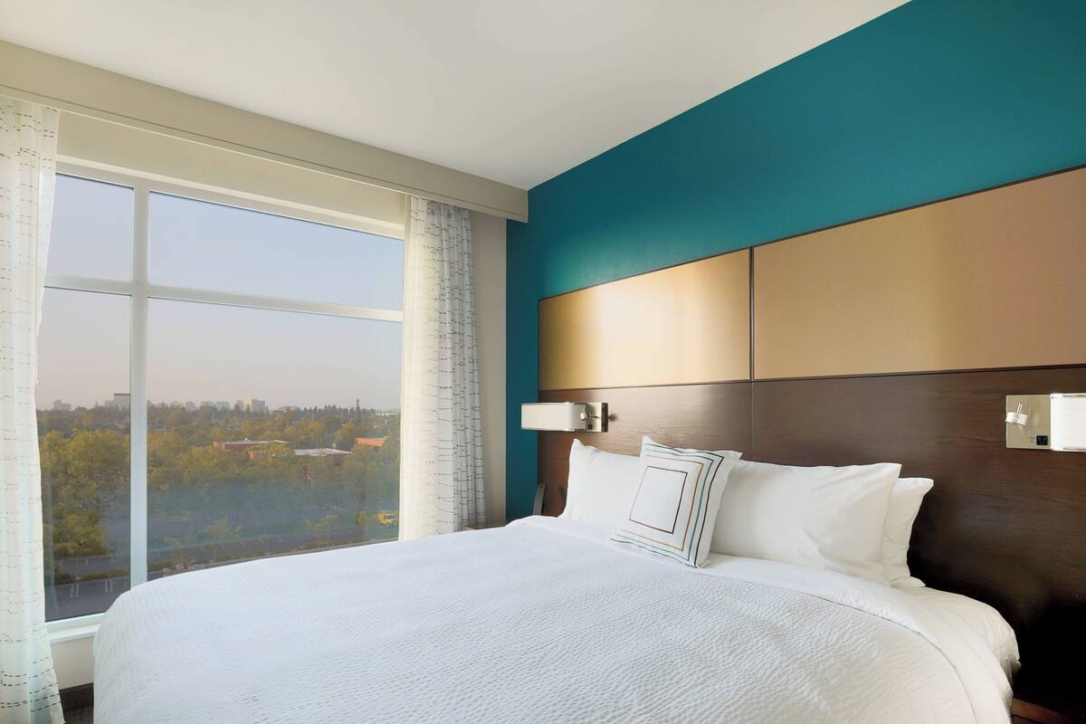 Une chambre d’hôtel avec un grand lit, une vue sur la ville et une tête de lit moderne.