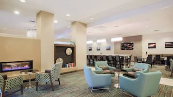 A hotel lobby with a fireplace, seating area, and a bar/lounge with tables and chairs.
