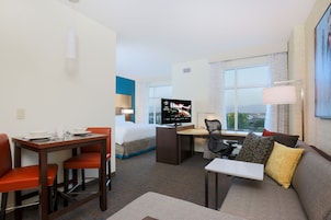 A hotel room with a bed, a desk, a TV, a sofa, and a window with a view.