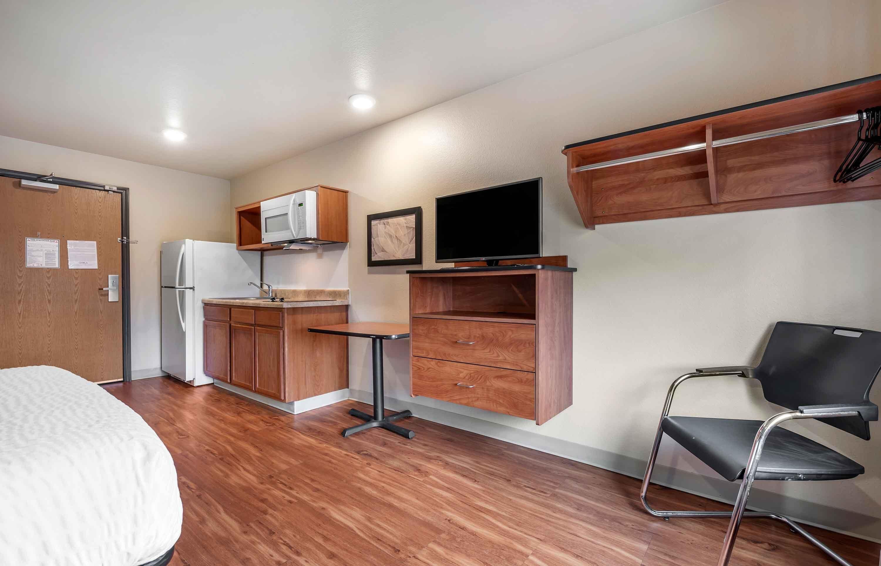 A compact room with a kitchenette, a bed, a desk with a chair, and a TV.