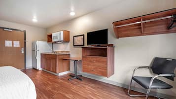 A compact room with a kitchenette, a bed, a desk with a chair, and a TV.