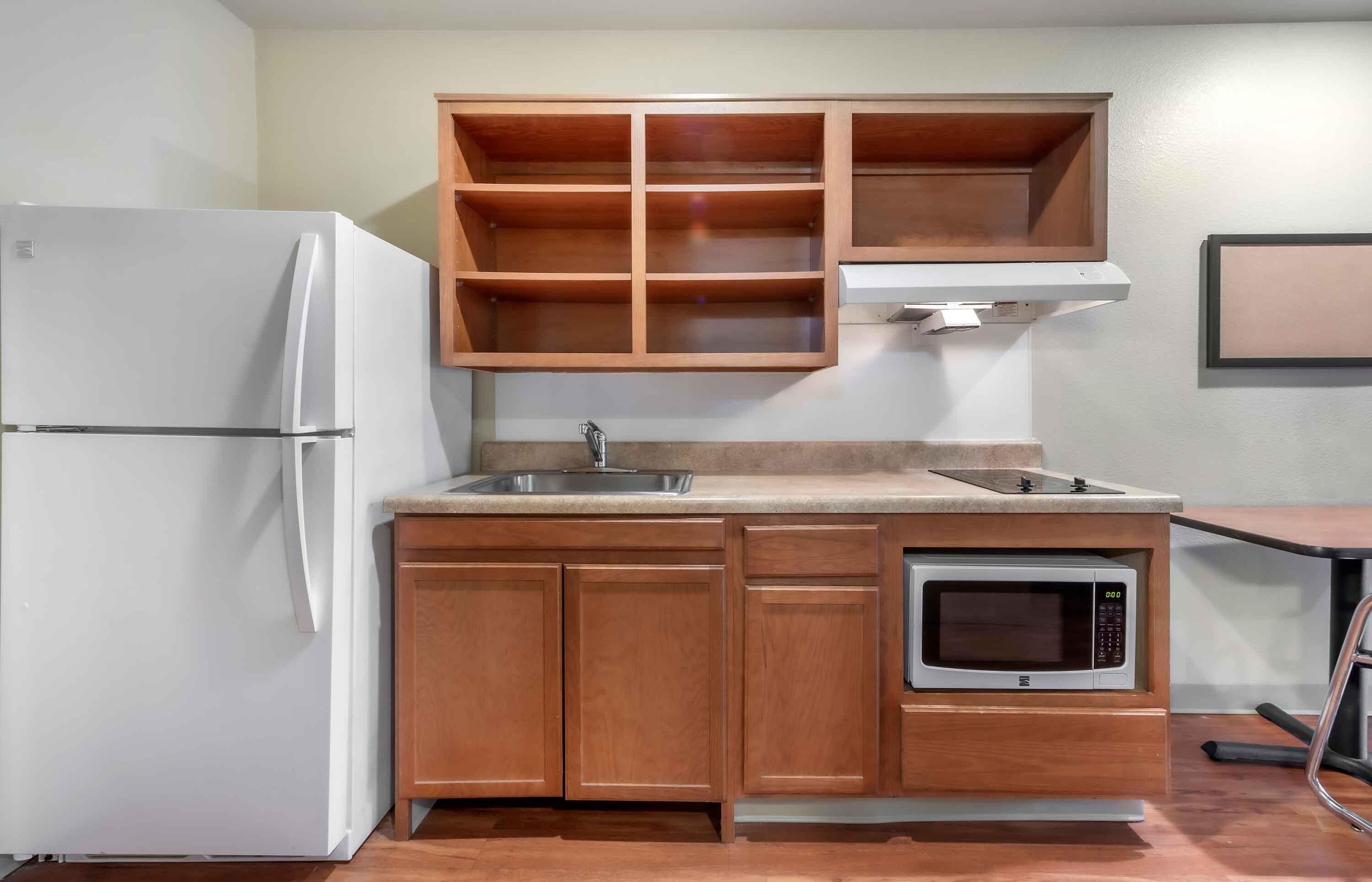 A compact kitchen with a built-in refrigerator, a microwave, wooden cabinets, and a sink.