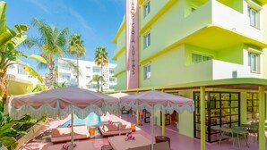 A hotel with a pool area featuring sun loungers and umbrellas, surrounded by palm trees and a clear blue sky. - Tropicana Ibiza Suites - Adults Only (Sant Josep de sa Talaia)