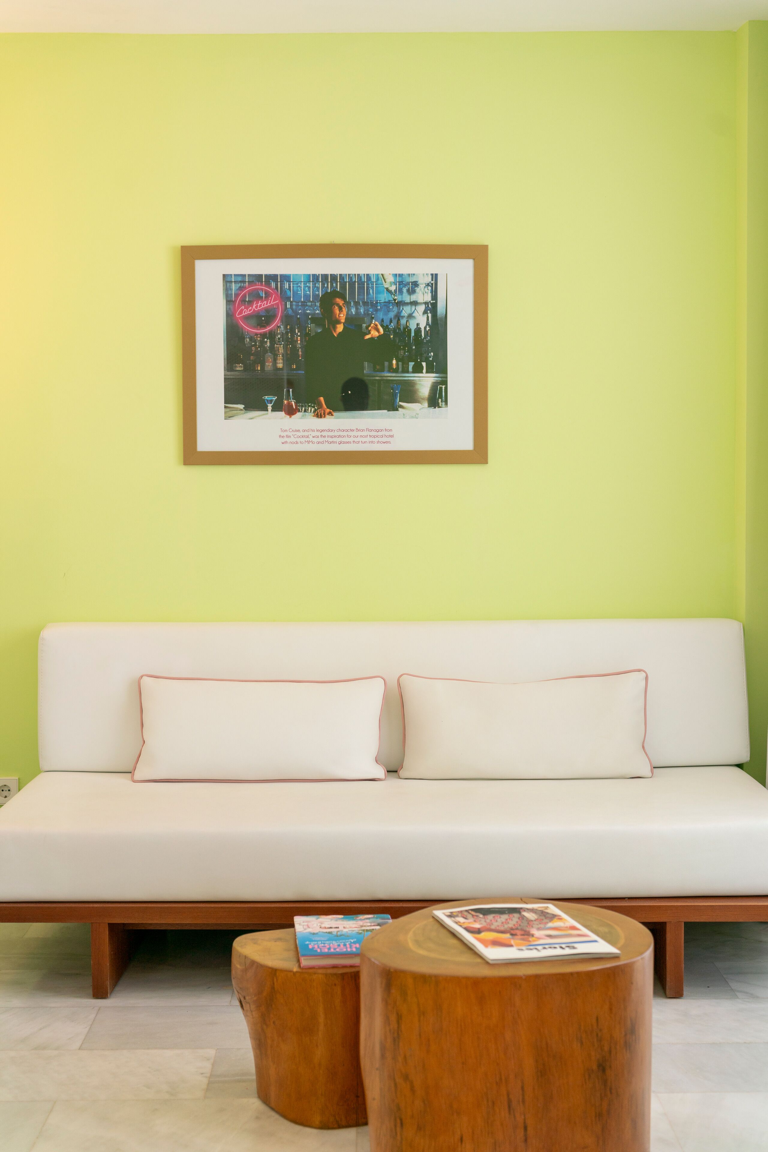 Una sala de estar moderna con una pared verde claro, un sofá blanco con dos cojines y dos mesitas de noche de madera.