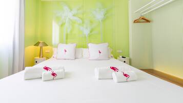 Habitación de hotel con cama, almohadillas blancas, mesita de noche, lámpara y un diseño de palmera en la pared.