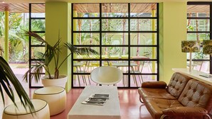 A modern living room with a brown leather sofa, a white coffee table, and a large window with a view of tropical plants. - Tropicana Ibiza Suites - Adults Only (Sant Josep de sa Talaia)