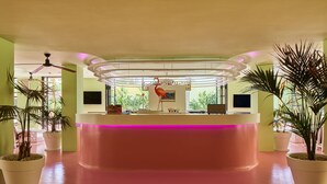 A reception area with a pink reception desk, ceiling fans, and potted plants. - Tropicana Ibiza Suites - Adults Only (Sant Josep de sa Talaia)