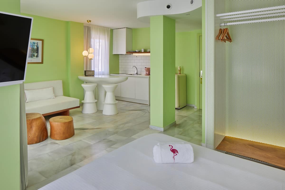 Quarto de hotel moderno com cama, sofá, pequena cozinha e banheiro.