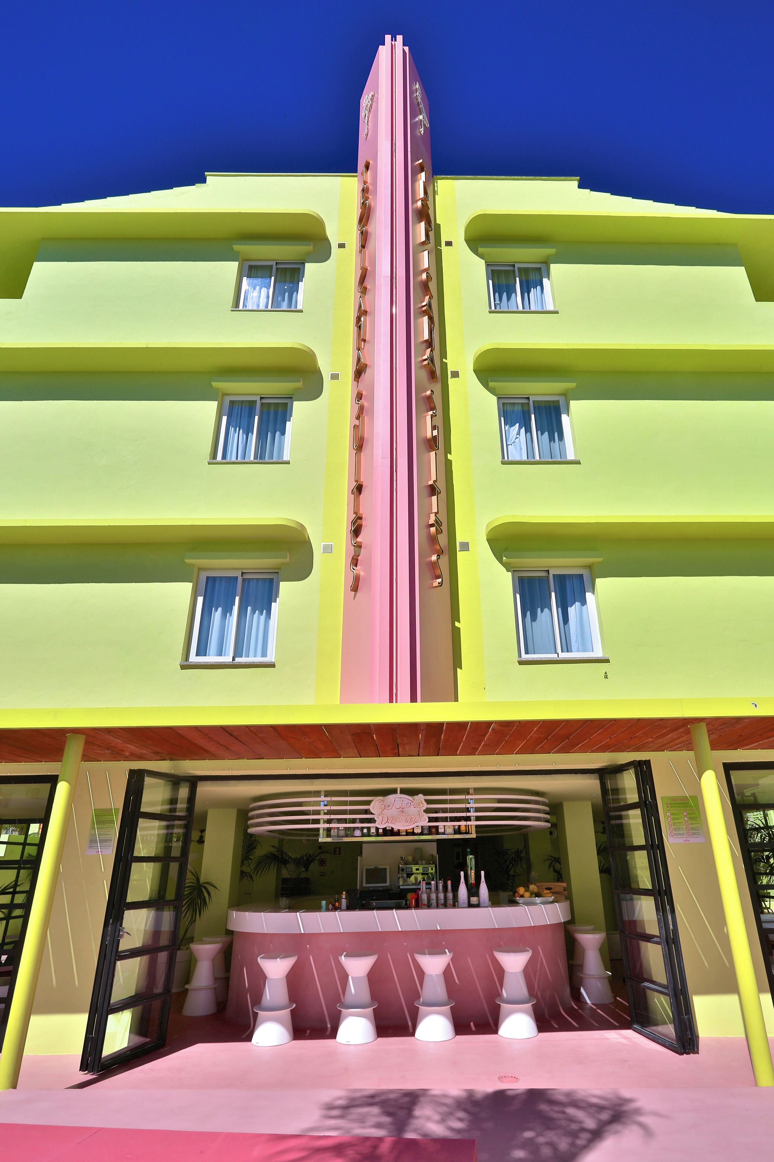 A multi-story building with a central pink and yellow facade, featuring a bar area with white stools and a counter.