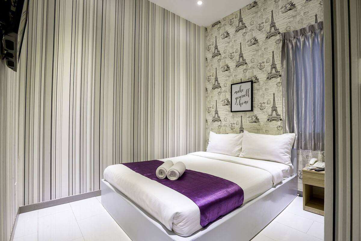 Ein Hotelzimmer mit einem Bett, Streifen-Tapete, einem gerahmten Zitat an der Wand und einem Fenster mit Vorhängen.