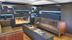 Een moderne woonkamer met een open haard, een bank, een salontafel en boekenkasten met decoratieve objecten.