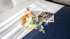 Een net opgemaakt bed met een tijdschrift, een bloemenboeket en een klein cadeautje.