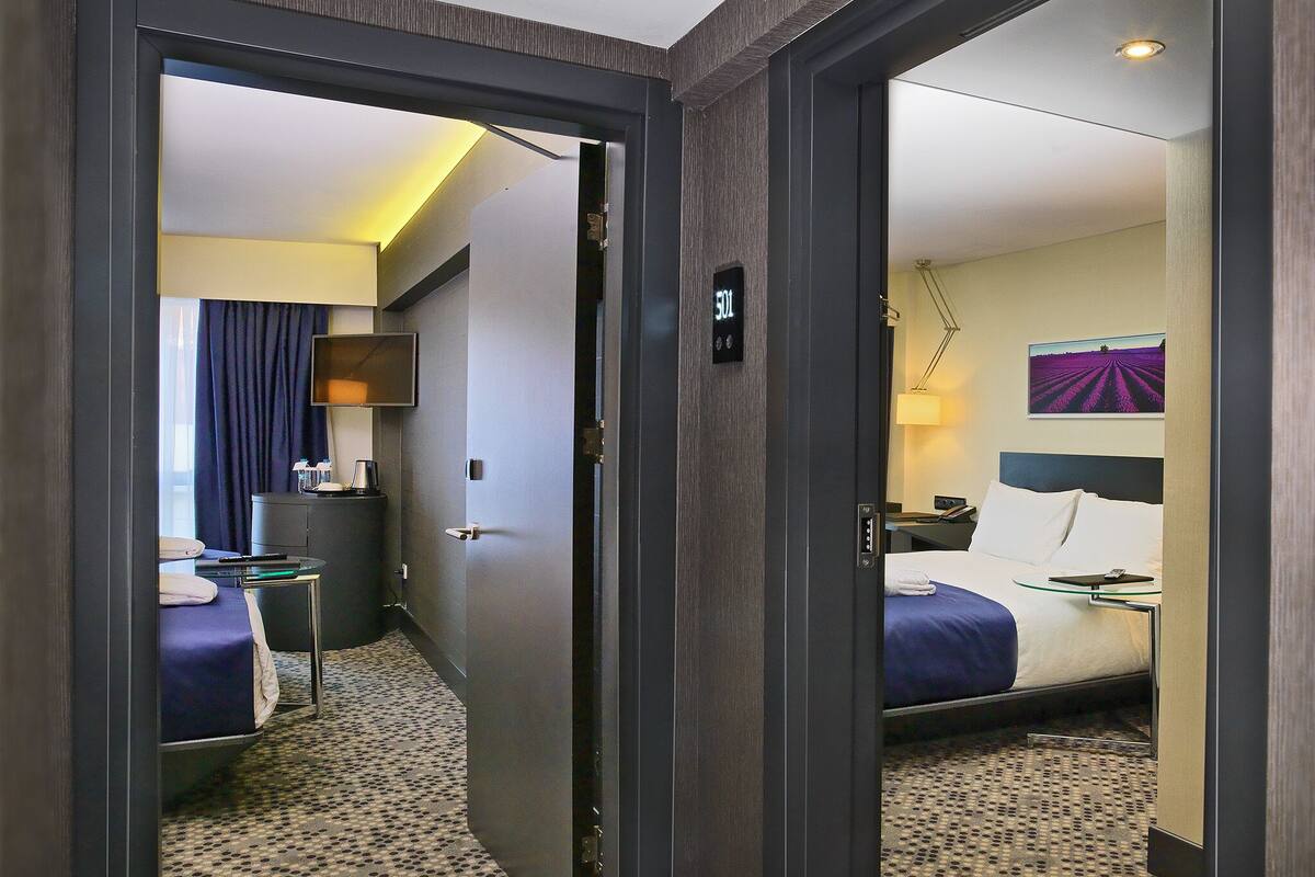 A hotel room with a bed, bedside table, lamp, and a view of a field through a window.