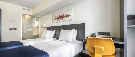 A hotel room with two beds, a desk, a chair, a phone, and a wall-mounted artwork.