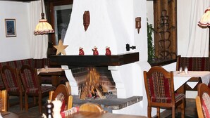 Interior acogedor de un restaurante con mobiliario de madera, chimenea y elementos decorativos como una estrella y figuritas rojas.