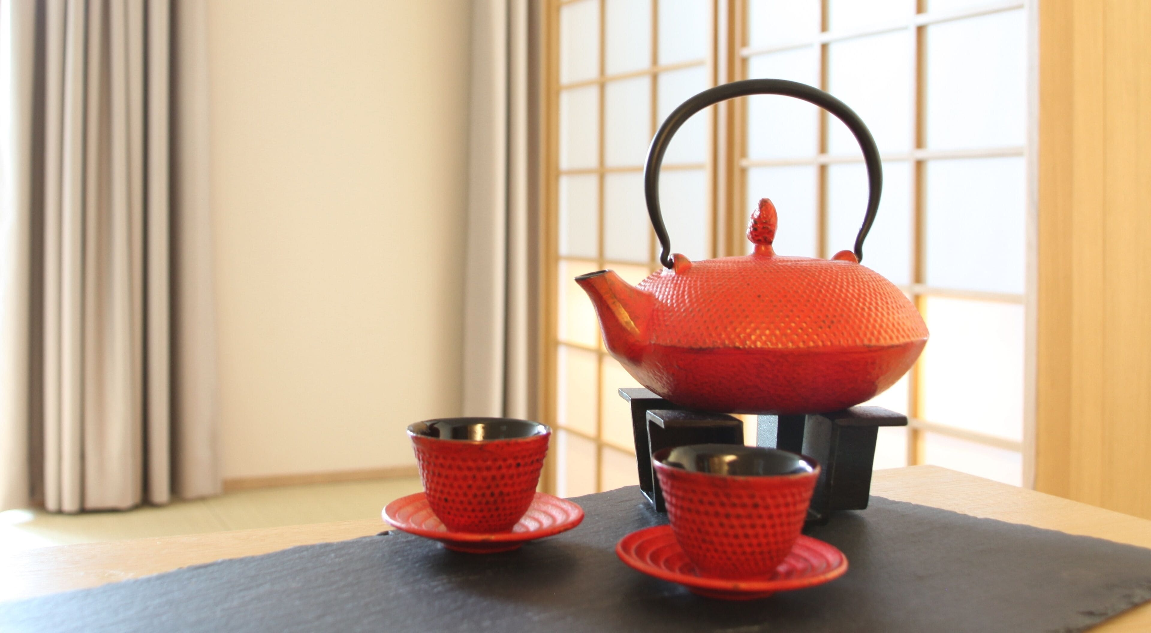 Una tetera roja sobre un pedestal negro con dos tazas a juego sobre una alfombra negra.