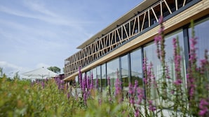 A modern building with large glass windows and a wooden deck. - Hotel Bora HotSpaResort (Radolfzell am Bodensee)
