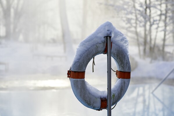 A lifebuoy covered in snow, attached to a metal pole, with a blurred background of a snowy landscape.
