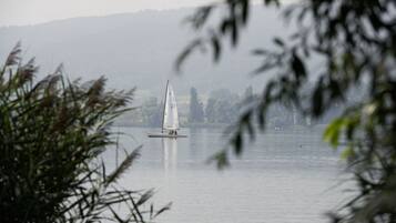 Ein Segelboot auf einem stillen See vor einer bewaldeten Hügelkulisse.