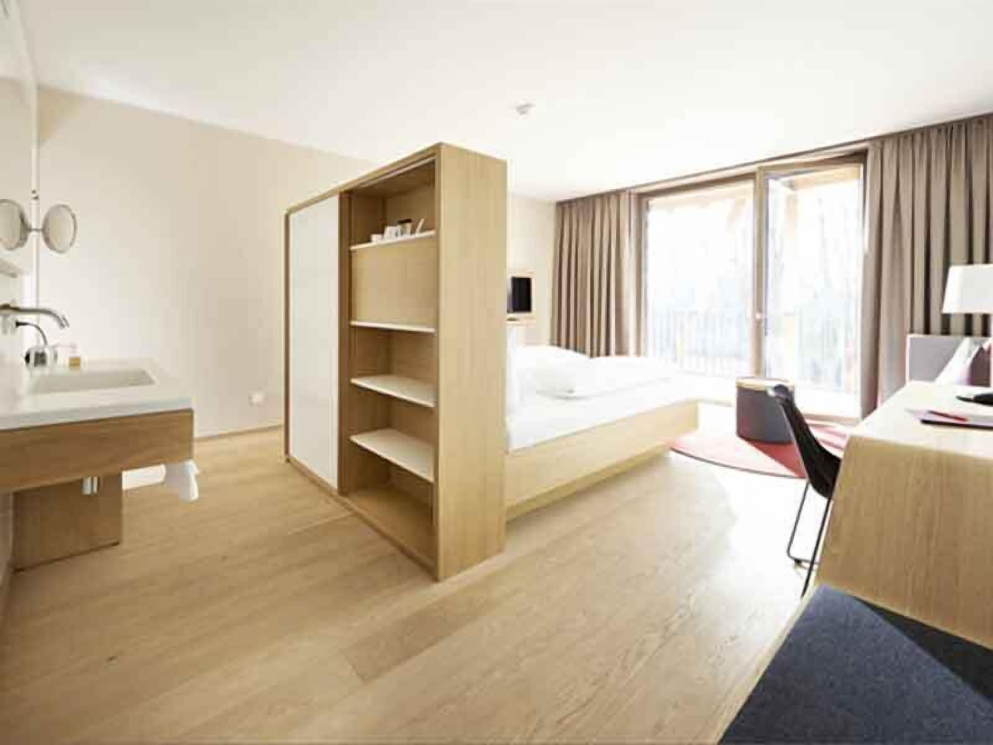 A hotel room with a bed, a desk, a chair, a wardrobe, a mirror, and a window.