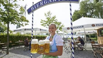 Eine Frau hält drei Bierkrüge vor einem Schild, auf dem 'Biergarten' steht.