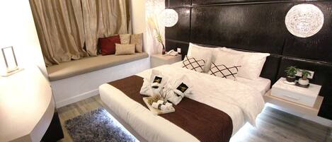 A modern bedroom with a bed, bedside tables, a window seat, and a large headboard.