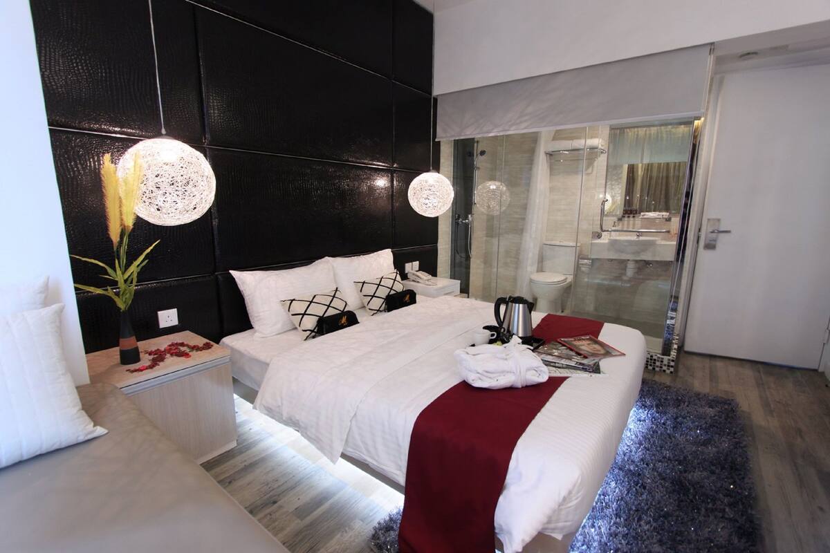 Un dormitorio moderno con una cama grande, mesitas de noche, zona de ducha con mampara de vidrio y una pared de acento roja.